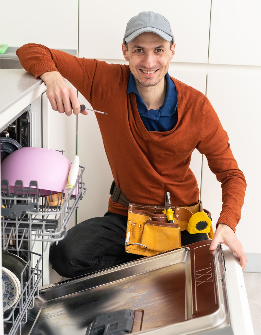 A man seated in a kitchen beside a dishwasher, illustrating appliance repair services in Houston, TX.
