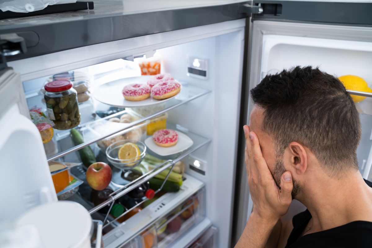 A man examines his refrigerator at home, contemplating potential appliance repair services for maintenance.