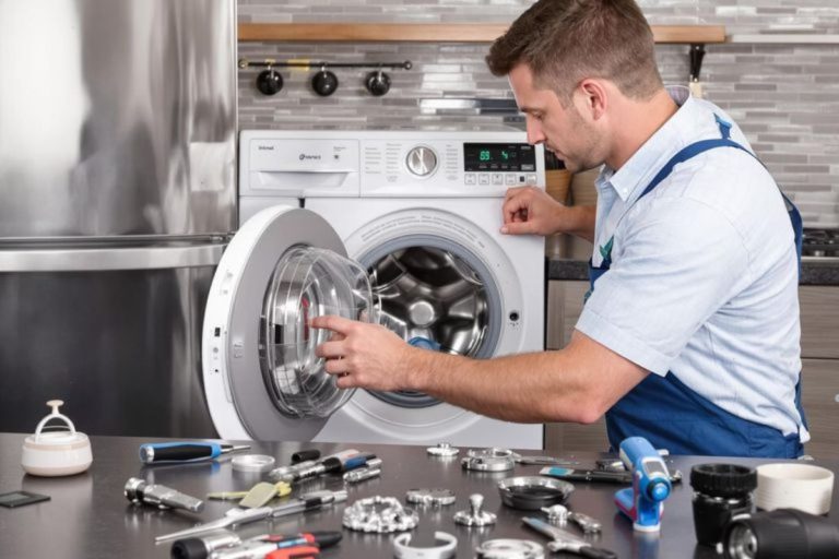 A man repairs a washing machine in a kitchen, showcasing professional appliance repair services in action.